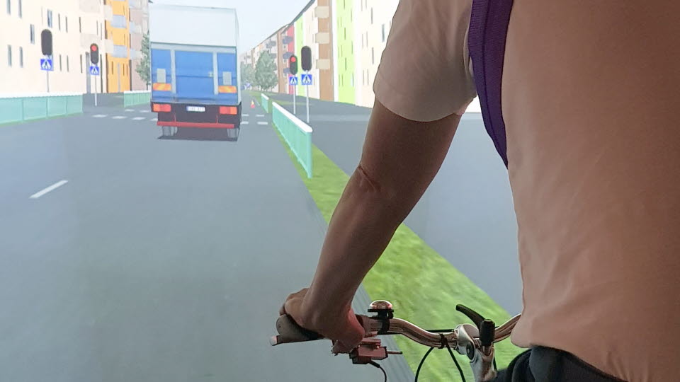 Person som cyklar i VTI:s cykelsimulator. Styre och arm syns i förgrunden, simulerad väg i bakgrunden.