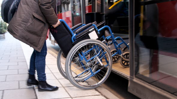 Person som kör in rullstol på en buss.