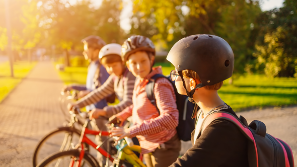 Fyra barn på sina cyklar, med cykelhjälmar och skolväskor.