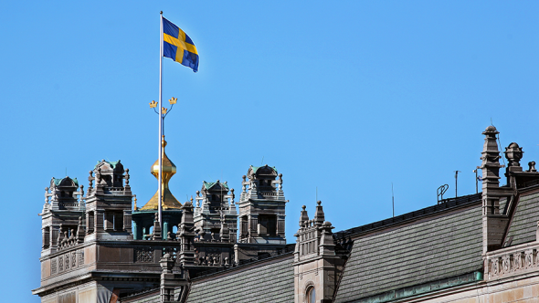 Taket på Rosenbad med Tre kronor och svenska flaggan mot blå himmel.