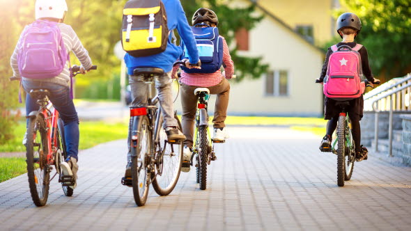 Fyra barn, tre pojkar och en flicka, i tioårsåldern på sina cyklar med ryggsäckar och cykelhjälmar. 