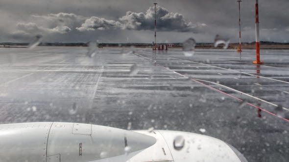 Flygfält en snöig dag. Del av flygplan syns i förgrunden.