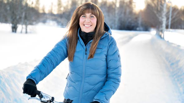 Porträttfoto av Hanna Forsberg med cykel på vinterväg i snöigt landskap.