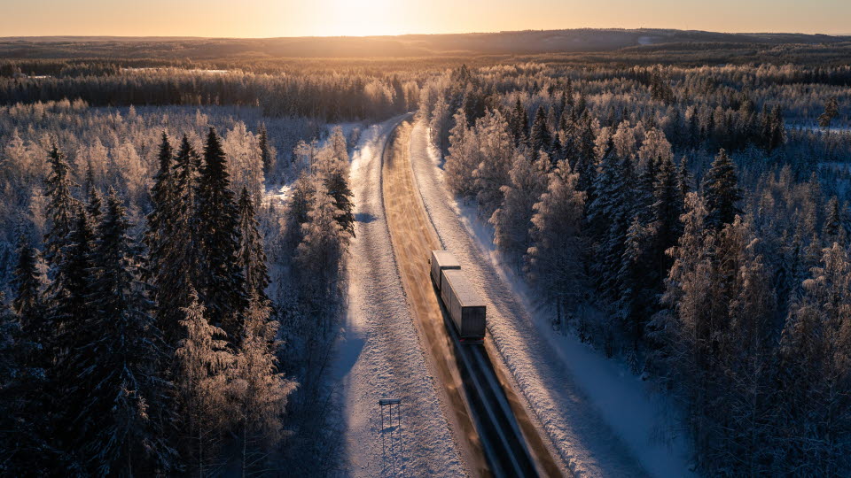 Lastbil på motorväg i vinterlandskap.