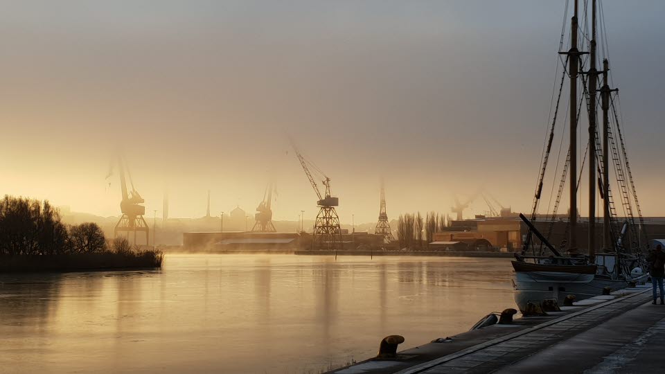 Lindholmen hamn i soluppgång. Lyftkranar syns på avstånd i dimma. 