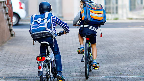Två skolpojkar cyklar till/från skolan med ryggsäckar och hjälmar.