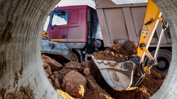 Grävskopa med jord- och bergmassor intill en lastbil.